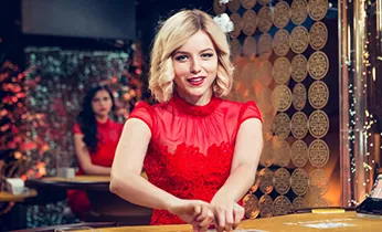 Hình ảnh một bình luận viên Campuchia đang tường thuật trận đấu đá gà trực tuyến trên màn hình lớn, với giao diện cá cược online phía dưới.